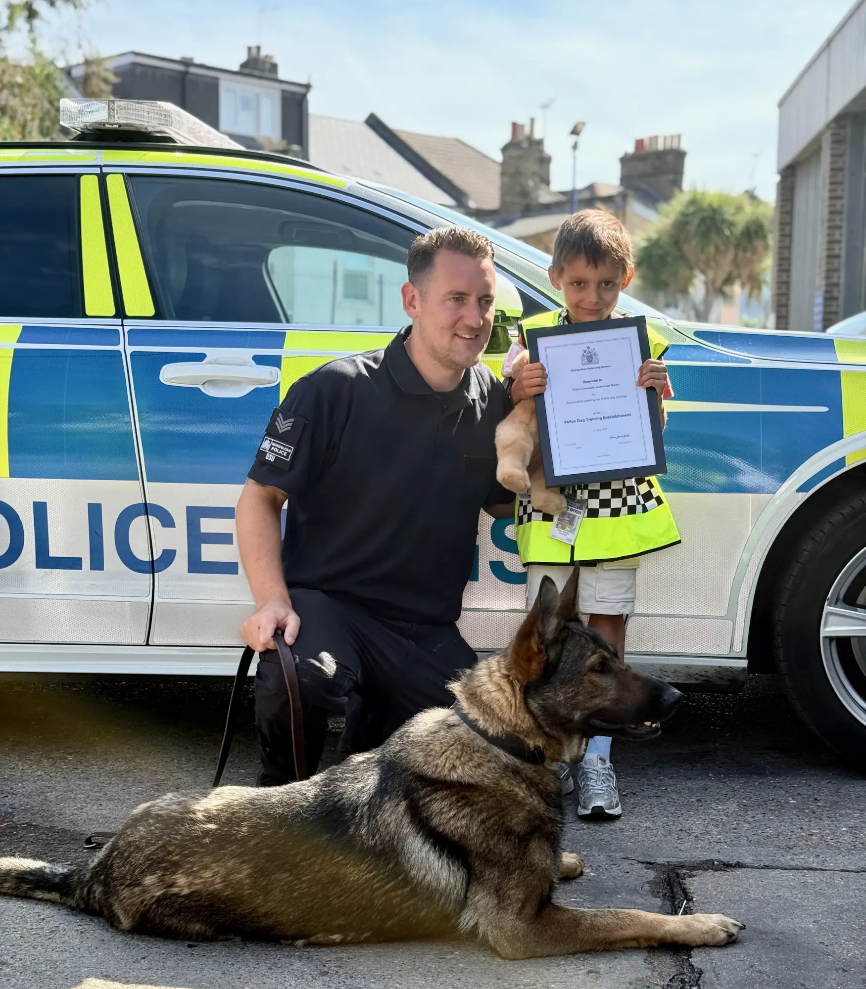 Certificate earned, posing proudly with a police German Shepherd in front of the Dog Section car. 🏅