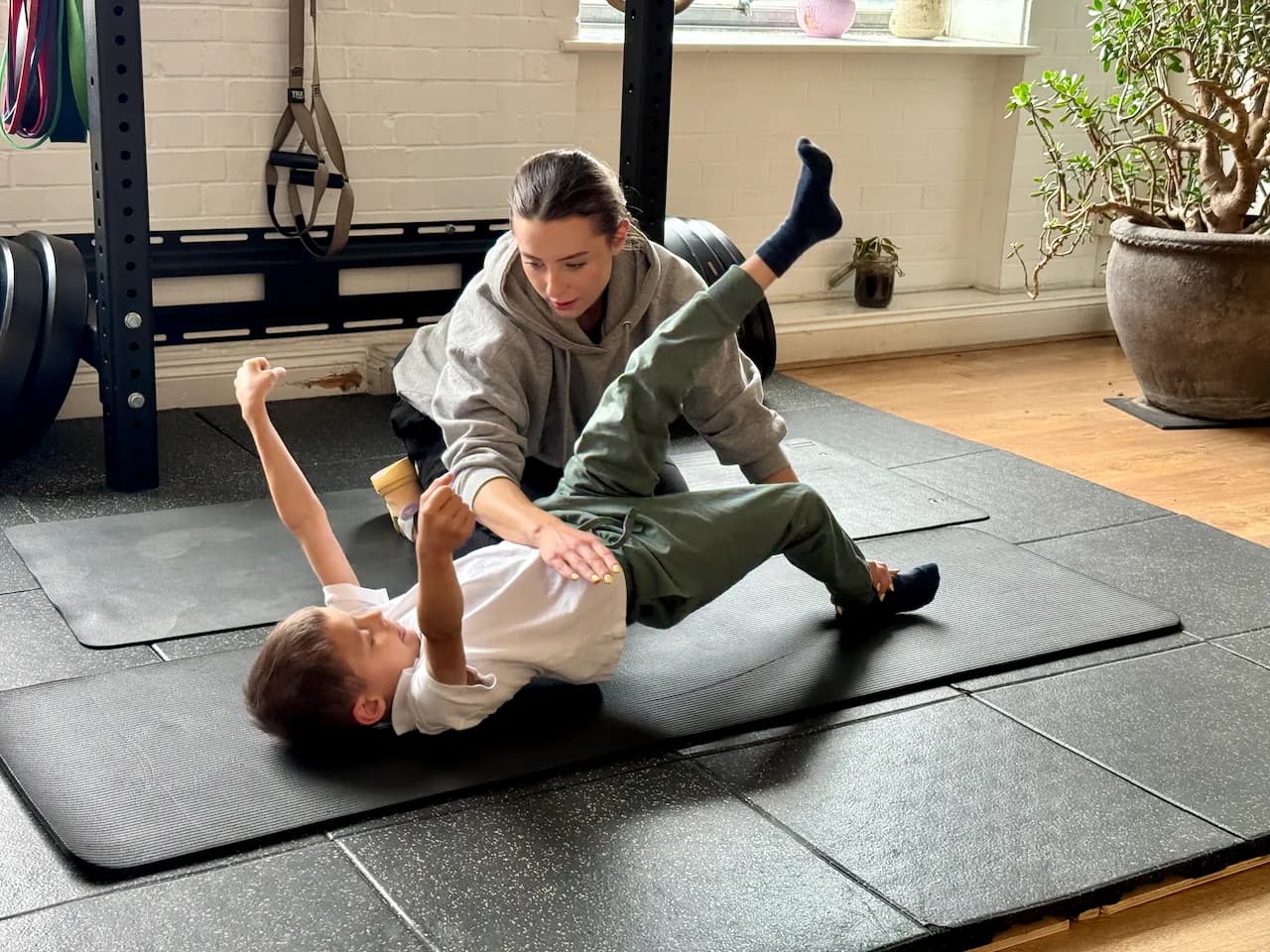 Single-leg work on the floor - Gabi guiding him through a knee-to-chest pull while he reaches with the opposite arm.